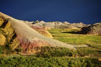 The evening sun paints the yellow mound area of the Badlands in brilliant colors with passing storm clouds as a backdrop.