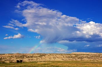A small raincloud with a rainbow dropping over the Palmer Creek Unit of Badlands National Park.