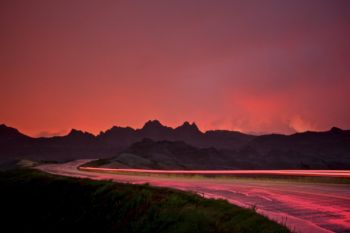 Red taillights of a passing car add to the red light of a summer storm at sunset.