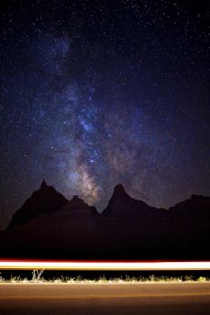 The milky way shining over the Scenic Loop Road illuminated by a passing vehicle.