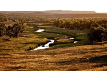 The setting sun paints the landscape golden. A side view of the wall is on the horizon with the Grand River in the foreground.