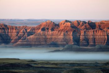 First light touching the Badlands with low fog at the foot of the formations.