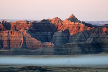 First light touching the Badlands with low fog at the foot of the formations.
