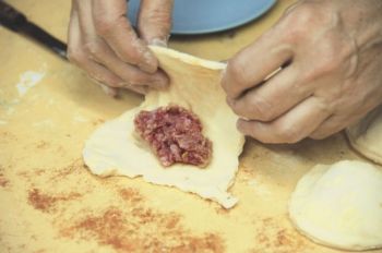 To form fleish kuchle, fold a square of rolled dough in half around the hamburger filling.